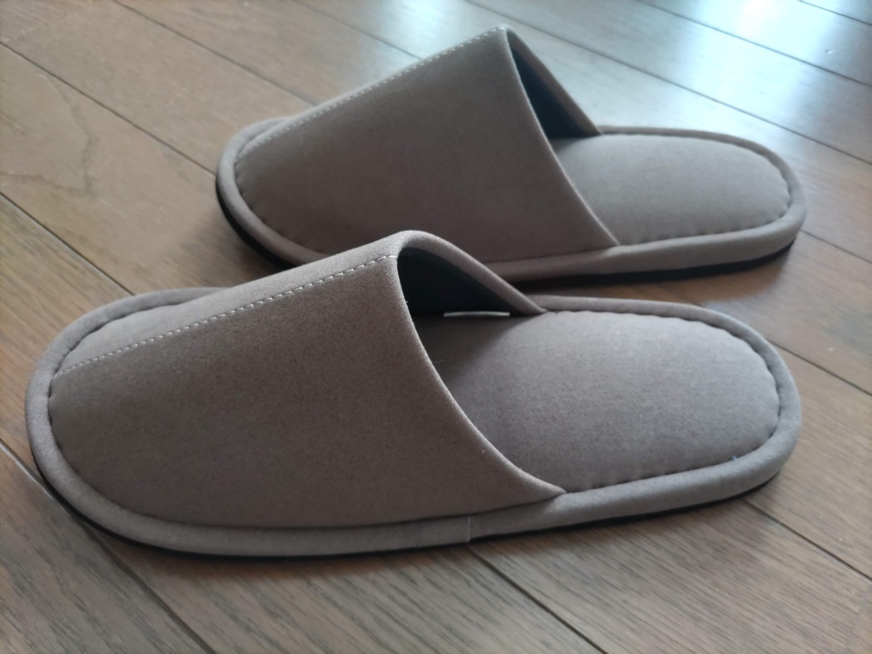 木目の床の上に置かれた、ブラウンの『匠のスリッパ』を横から撮影した写真。ふっくらした厚みと丁寧な縫製が見えるアングル。