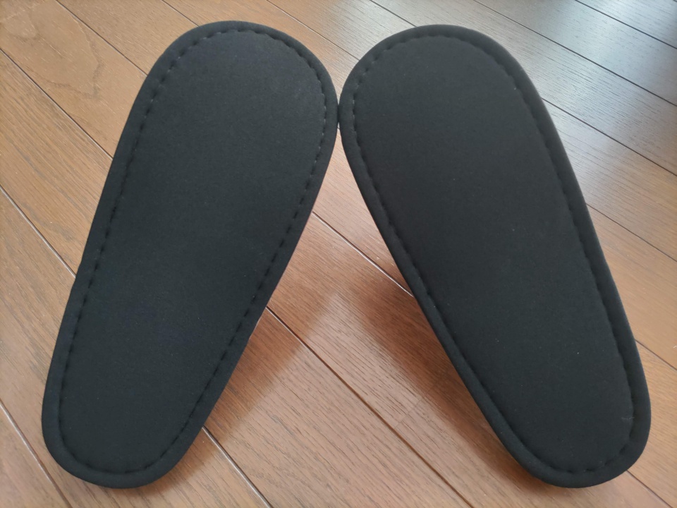 木目の床の上に置かれた、裏返した匠のスリッパのソール部分を写した写真。黒い底面と丁寧な縫製が確認できる構図。