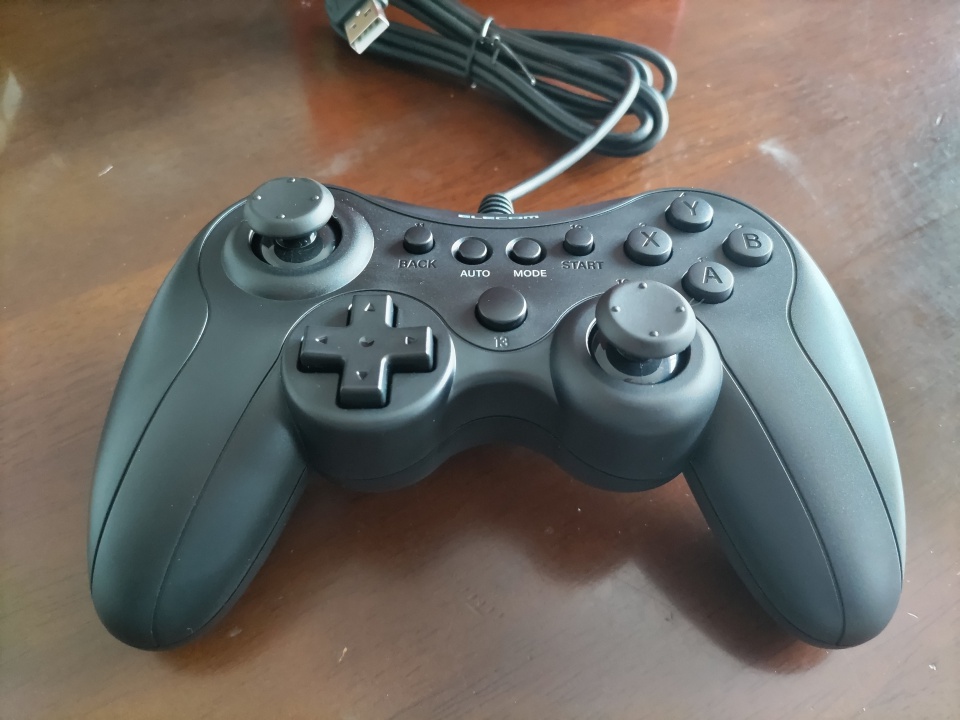 エレコムのゲームパッドGP20xを木目のテーブルの上に置いた写真。左右のアナログスティック、各ボタン、USBケーブルがはっきり写っている。