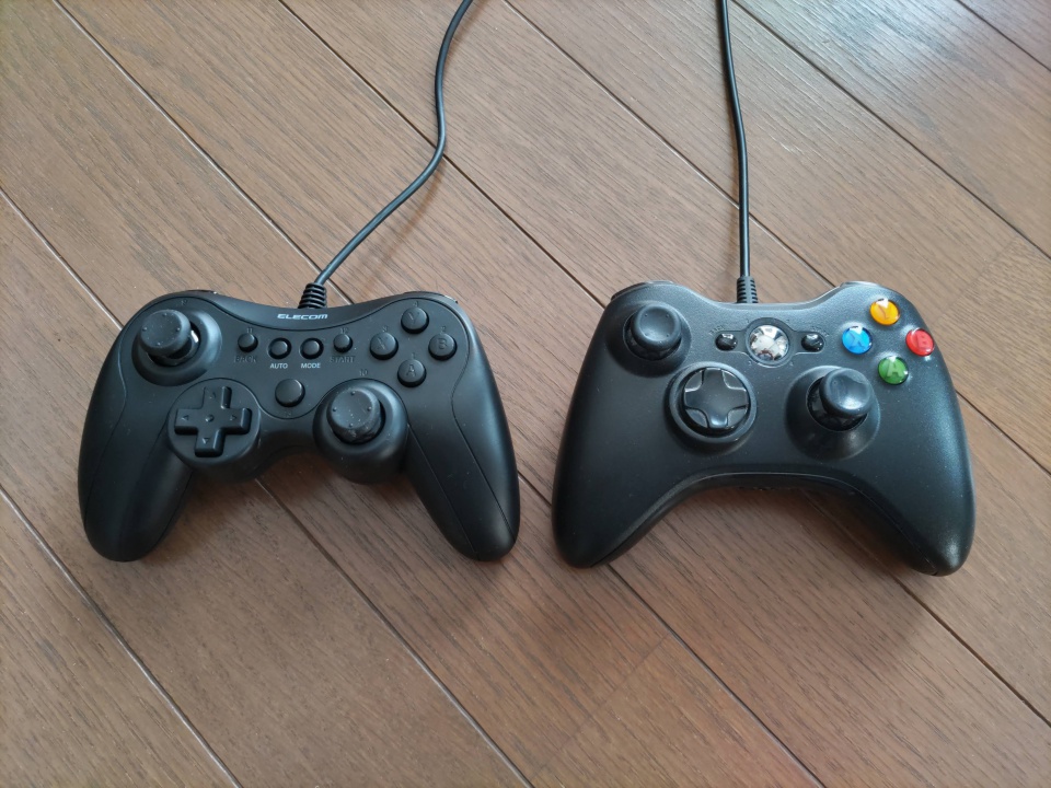 エレコムGP20x（左）とXbox360コントローラー（右）を木目の床の上に並べて撮影した写真。サイズや形状の違いがよく分かる構図。