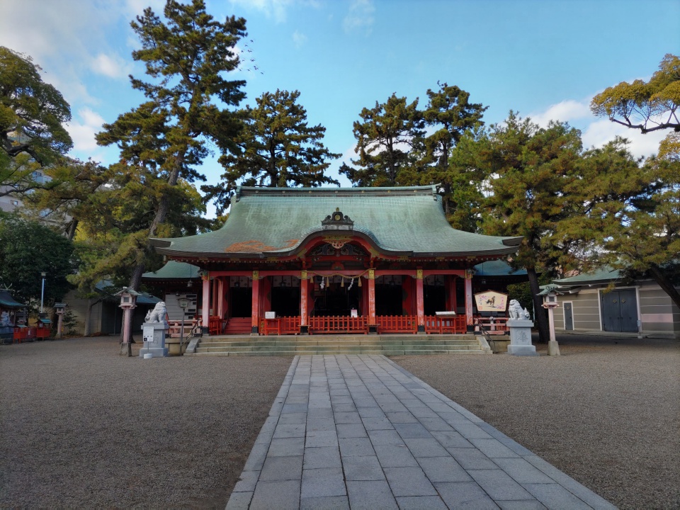 長田神社の拝殿を正面から撮影した写真。石畳の参道の先に朱色の拝殿が建ち、周囲には松の木が立ち並び、静かで穏やかな雰囲気が広がっている。