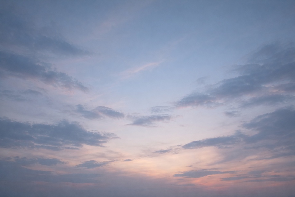 薄い青と淡いピンクに染まった夕暮れの空。雲がゆっくりと広がり、静かで余白のある時間を感じさせる空の風景。