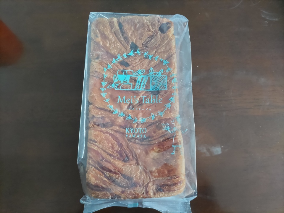 高級スイーツデニッシュ栗1斤を箱から取り出し、テーブルの上に置いた状態の写真。透明な包装越しに層のあるデニッシュ生地と栗入りの様子が見え、メイズテーブルのロゴが印刷されている。