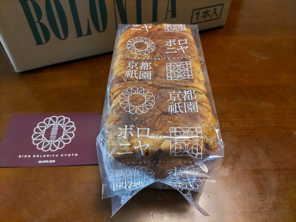 京都祇園ボロニヤの「はんなりデニッシュ キャラメルコーヒー」1斤を段ボール箱から取り出した状態で撮影した写真。透明袋越しにマーブル状のデニッシュ生地が見え、背後には「BOLONIYA」と書かれた専用の段ボール箱が置かれている。