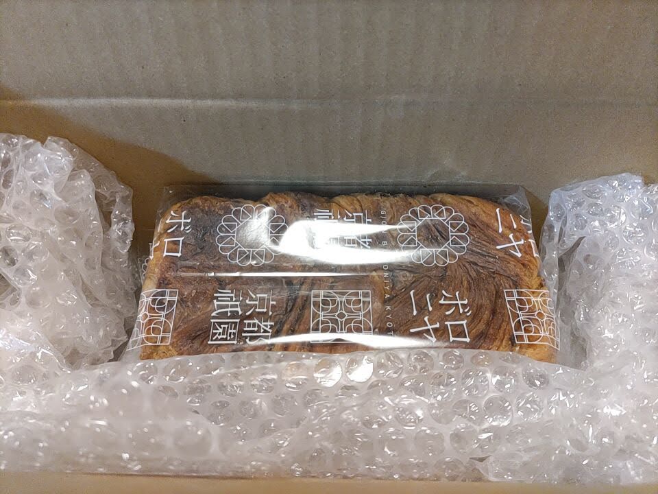 段ボール箱の中に入った京都祇園ボロニヤの「はんなりデニッシュ キャラメルコーヒー」1斤を撮影した写真。デニッシュは透明パッケージに包まれ、上下と両側を緩衝材（プチプチ）で保護されている様子が分かる。