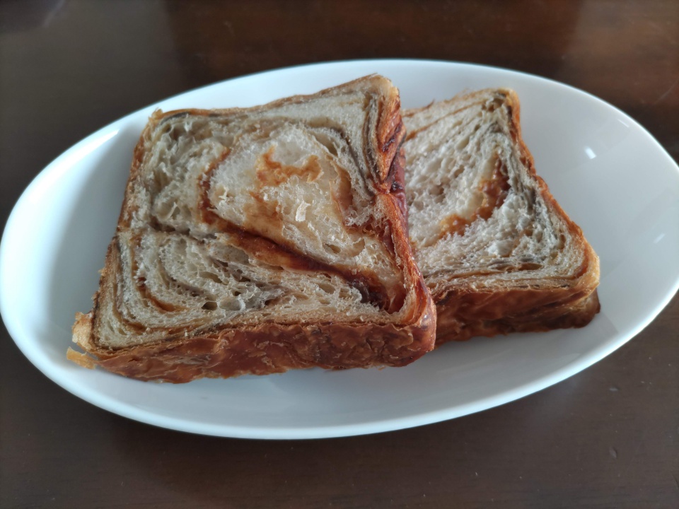 白い皿の上に並べた京都祇園ボロニヤ「はんなりデニッシュ キャラメルコーヒー」のスライス2枚。層が美しく重なったデニッシュ生地にキャラメルコーヒーのマーブル模様が広がり、焼き色のついた側面が食欲をそそる。