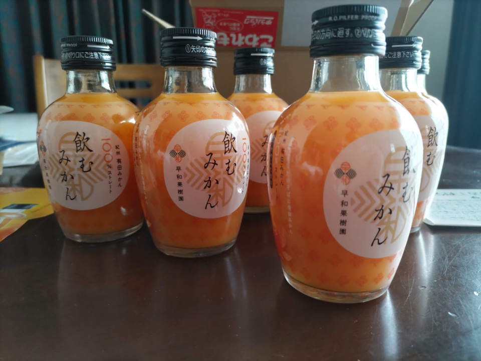 早和果樹園の飲むみかんの瓶を6本並べた様子。濃いオレンジ色のみかんジュースが入ったガラス瓶がテーブルの上に並んでいる。