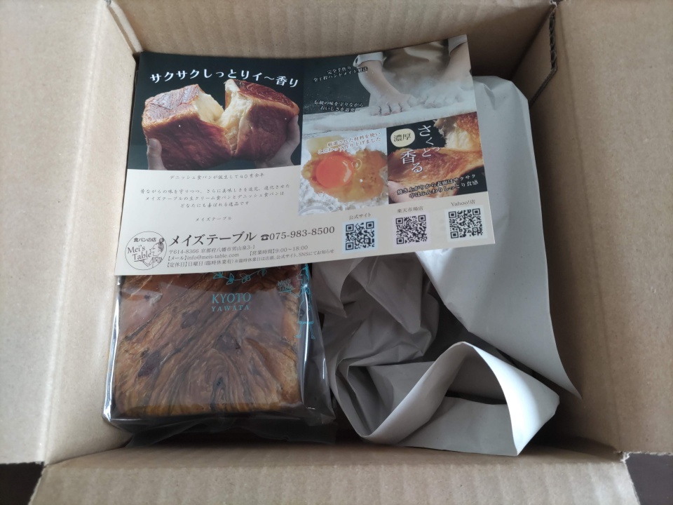 宅配で届いたメイズテーブルのスイーツデニッシュ「Wチョコ抹茶」1斤が入った箱を開封した様子。箱の中に包装されたデニッシュパンと商品案内のチラシ、緩衝紙が入っている。