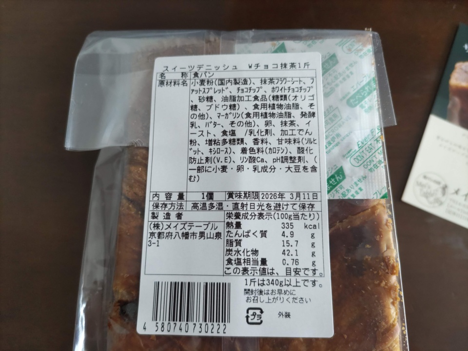 メイズテーブルのスイーツデニッシュ「Wチョコ抹茶」1斤の原材料表示ラベルを撮影した写真。包装袋の上から原材料名、内容量、賞味期限、栄養成分表示などが記載されたラベルが確認できる。