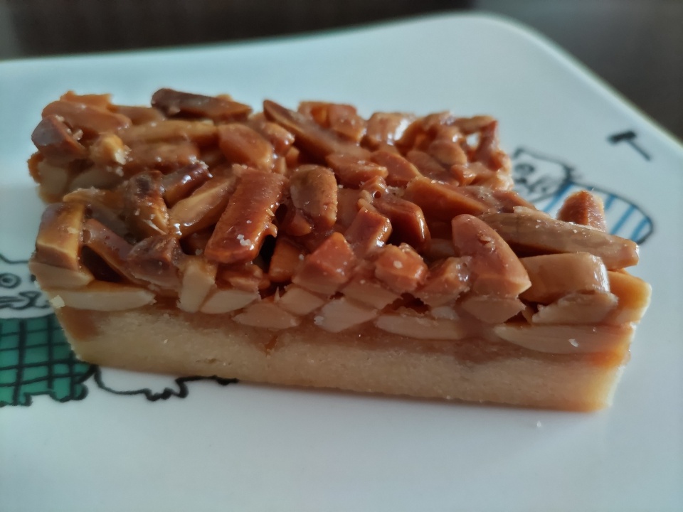 ケーキハウスカネヤマのアマンディーヌを白い皿に盛り付けた写真。キャラメリゼされたアーモンドがたっぷりのった香ばしい焼き菓子。