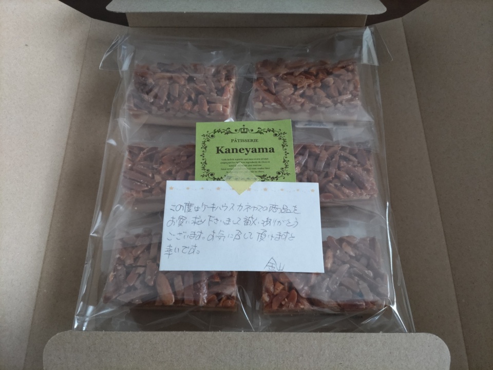 ゆうパケットの箱を開封した直後の写真。ケーキハウスカネヤマのアマンディーヌが透明袋に個包装されて箱の中に並び、手書きのメッセージカードが添えられている。