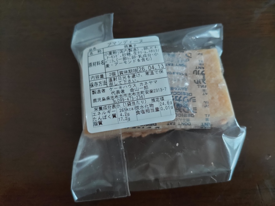 ケーキハウスカネヤマのアマンディーヌ個包装の裏面ラベル。原材料名、賞味期限、栄養成分表示などが記載されたシールが貼られている。