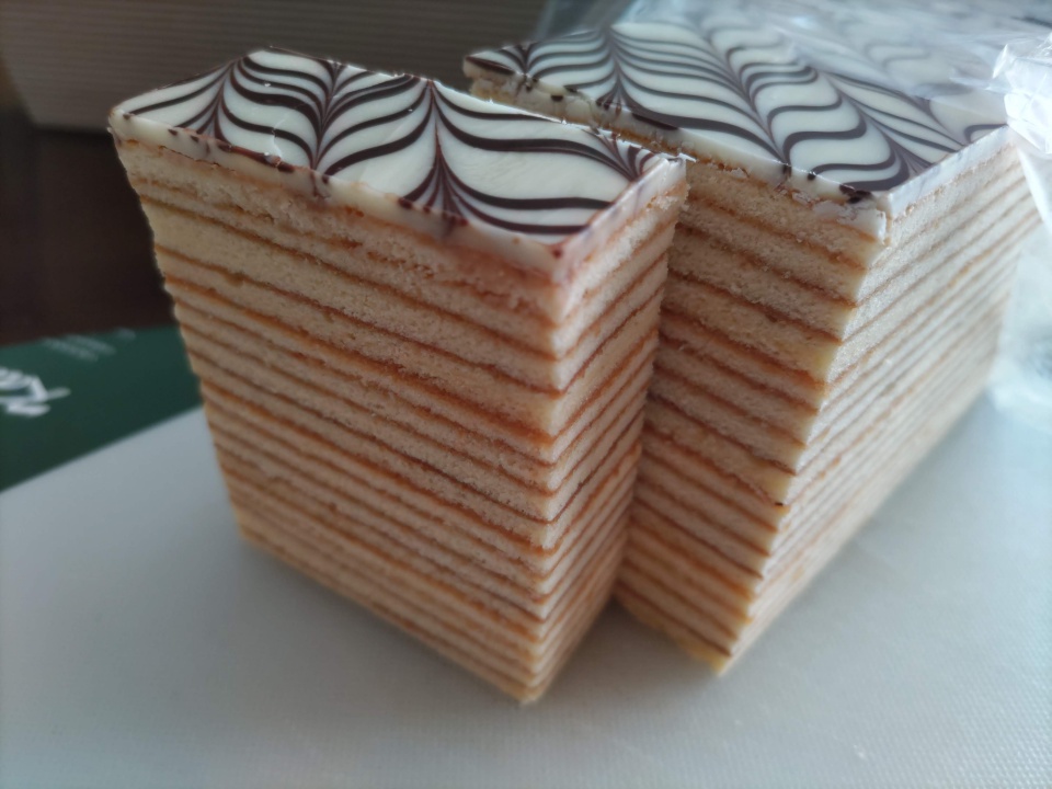 志布志金山バームを一切れカットした直後の写真。16層にも重なったしっとりした生地の断面が美しく、上部には白とチョコの矢羽根模様のコーティングが施されている。切り分けた2つの断面が並び、層の細かさと厚みが際立っている。