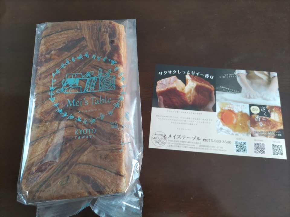 透明な袋に入った桜餡デニッシュと、メイズテーブルの紹介チラシを並べてテーブル上に置いた様子。