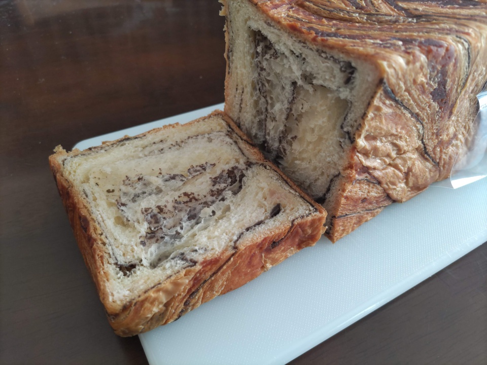 桜餡デニッシュを切り分けた直後の写真。まな板の上に1斤とカットした1枚を並べ、断面からこし餡とバターの層が見えている。