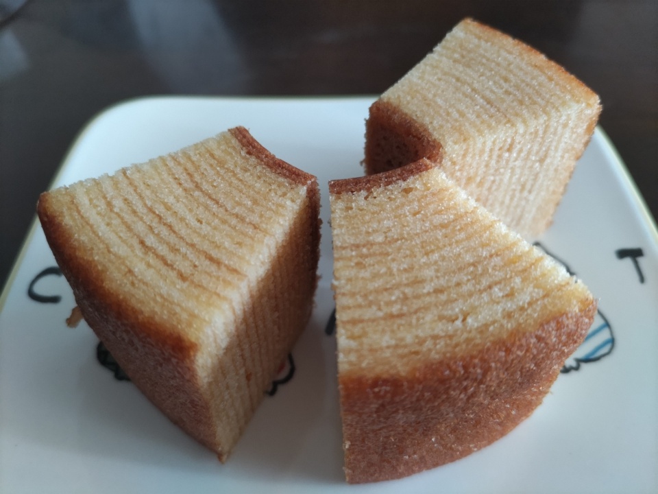 山田養蜂場のはちみつバウムを3切れにカットし、白いお皿に盛り付けた写真。しっとりとした層が重なった断面が見え、外側はこんがりと焼き色がついている。