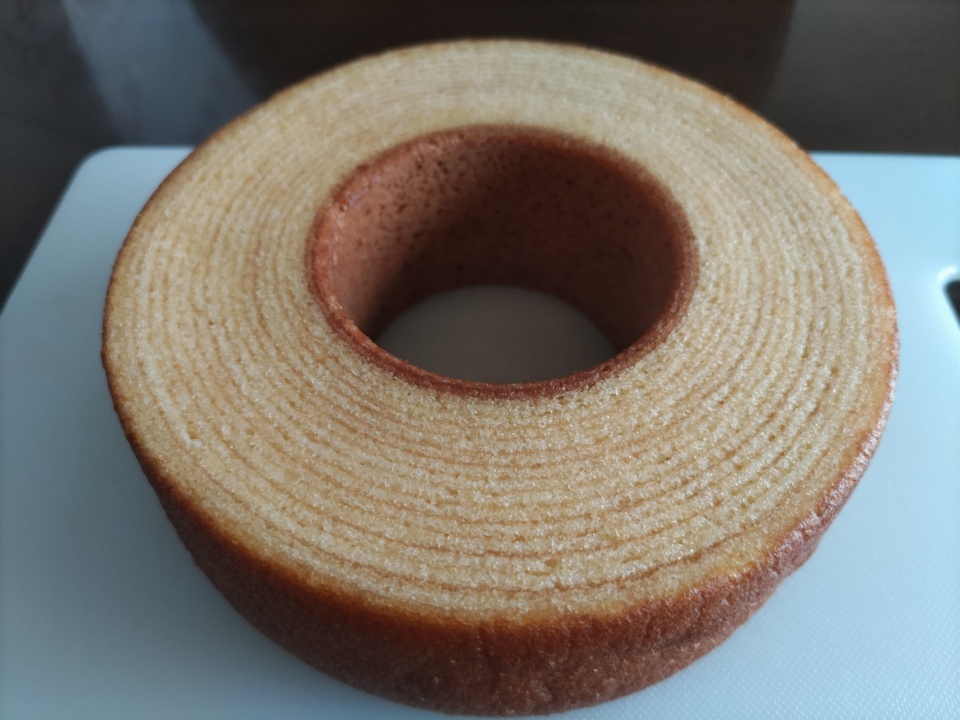 まな板の上に山田養蜂場のはちみつバウムを丸ごと置いた状態で撮影した写真。しっとりとした層が重なった断面と、こんがりと焼き色のついた外側がはっきり確認できる。