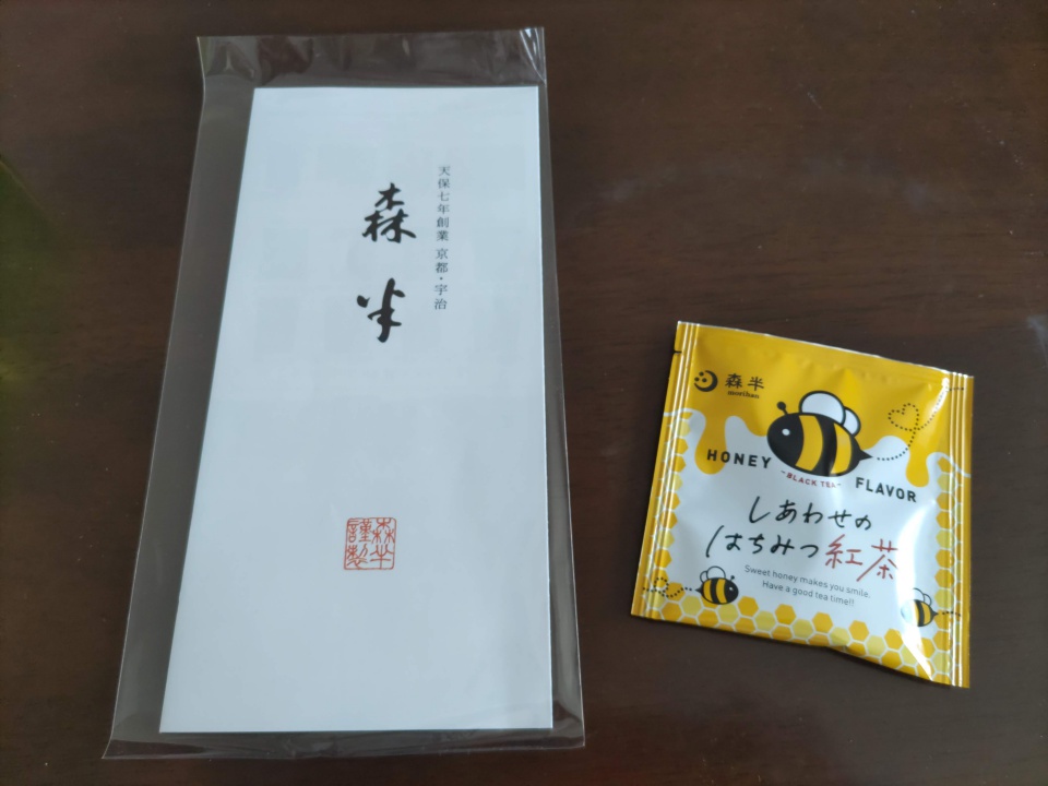 森半のリーフレットと、おまけで付属していたはちみつ紅茶1パックの写真。リーフレットは透明袋入りで、隣に黄色いパッケージの紅茶が置かれている。