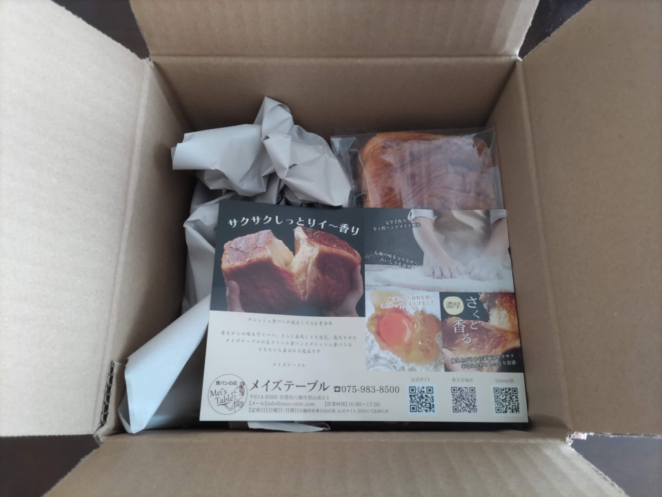開封したダンボール箱の中に、緩衝用の紙と一緒に瀬戸内レモンデニッシュが入っている様子。上には商品紹介のチラシが置かれ、右上に個包装されたデニッシュが見える。