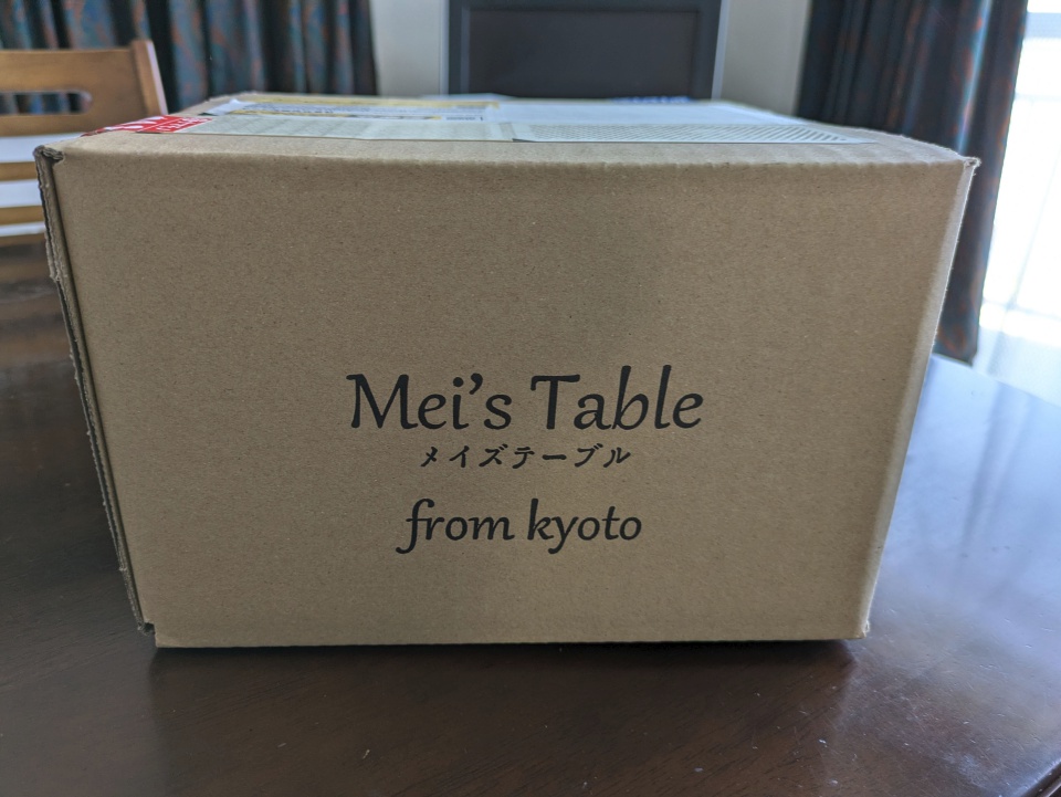 メイズテーブルから届いた宅配用ダンボール箱の写真。箱の正面には「Mei’s Table（メイズテーブル） from kyoto」のロゴが印刷されており、濃厚ピュアチョコレート1斤の開封前の様子が写っている。