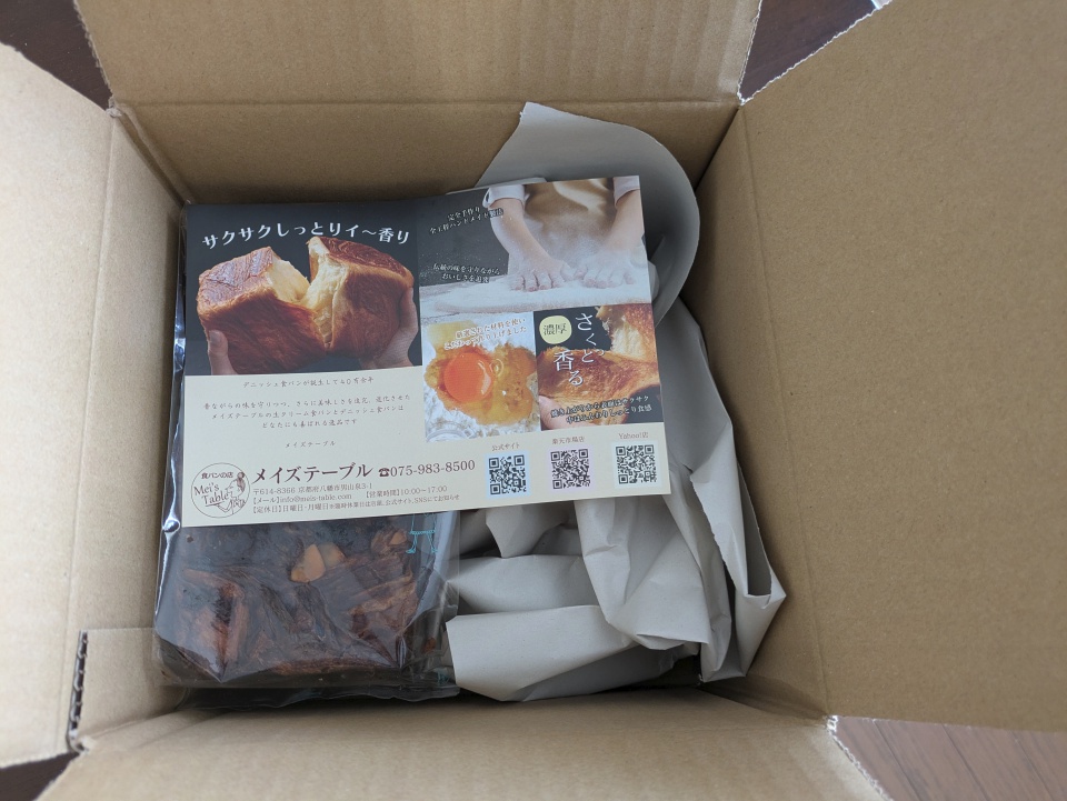 メイズテーブルから届いた宅配ダンボールを開封した直後の写真。箱の中には「濃厚ピュアチョコレート1斤」が包装された状態で入っており、パンフレットや緩衝用の紙と一緒に丁寧に梱包されている。